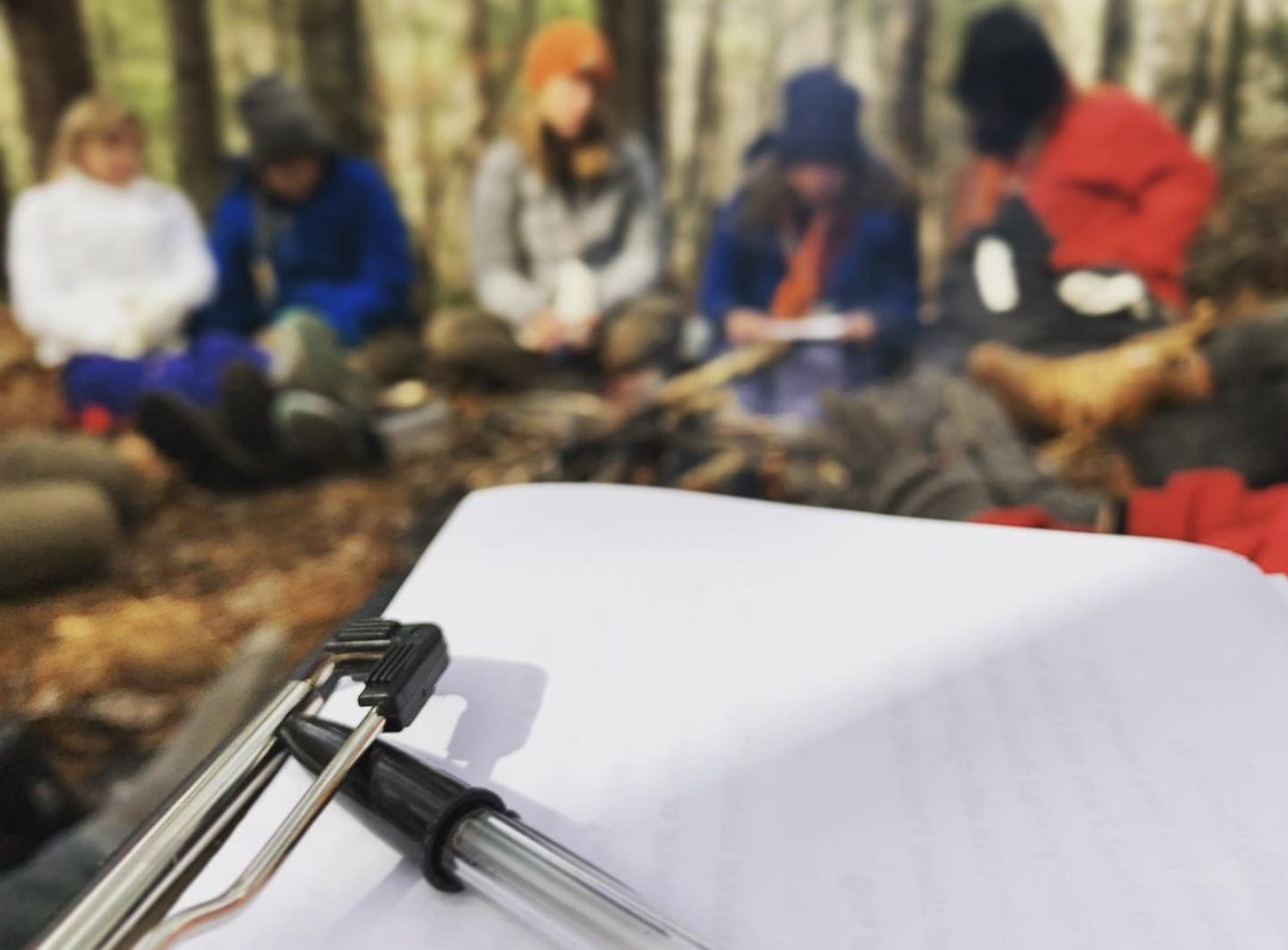 Picture of students sitting in the wilderness with a clipboard for schoolwork.